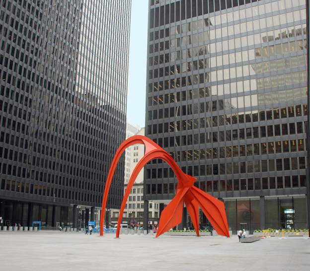 Photo of the Chicago Federal Center Courtyard. Three large, black, modern building surround the sides, with a bright red arched modern sculpture serving as the focal point of the courtyard. Taken by Massiel Lucca-Amador (5P1FB).