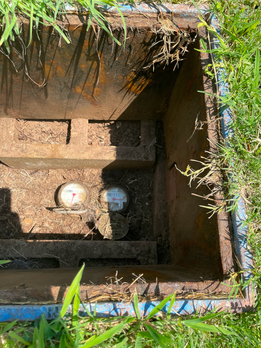 Photo of a hole in the lawn with metal sides. Two water meters and two cinderblocks are visible at the bottom.