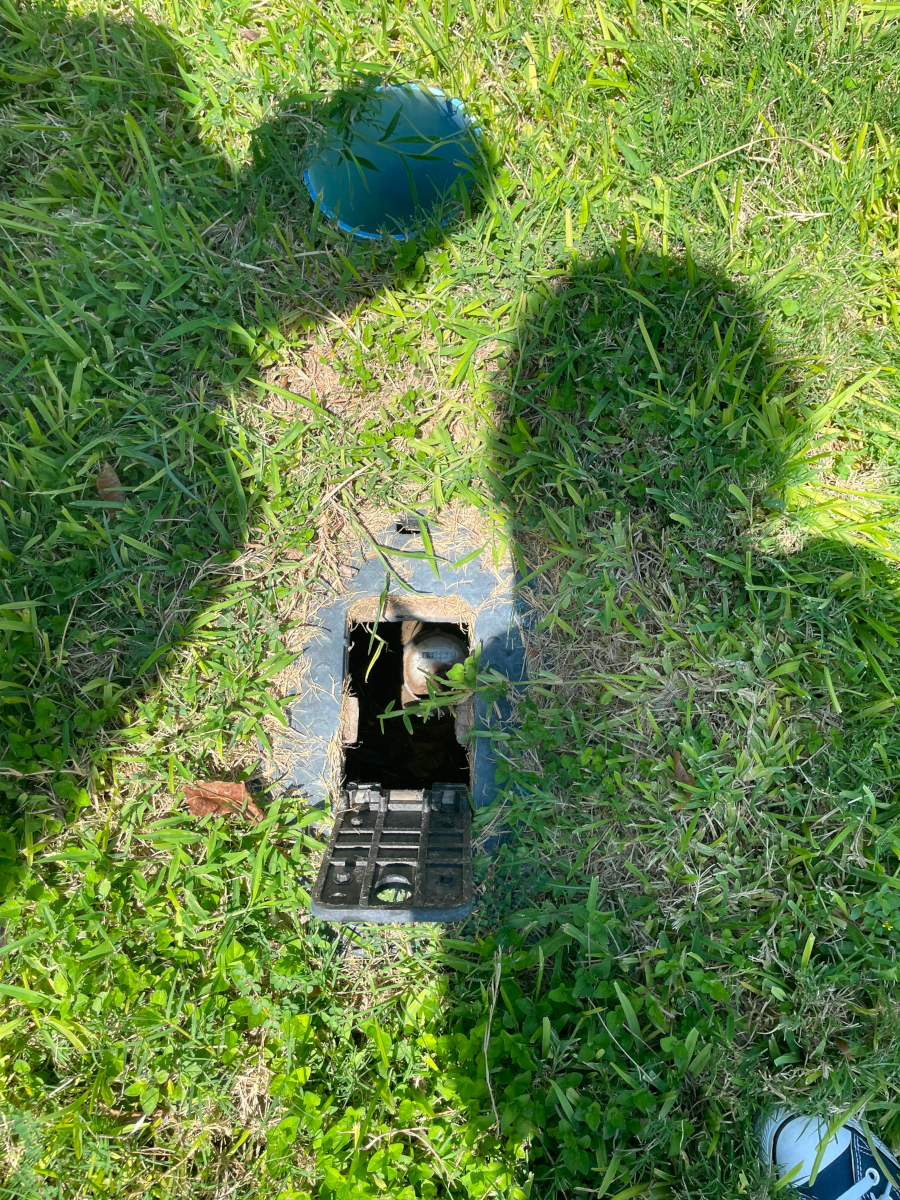 Photo of a small hold in a lawn with an open hatch. A single water meter is just visible through the hole.