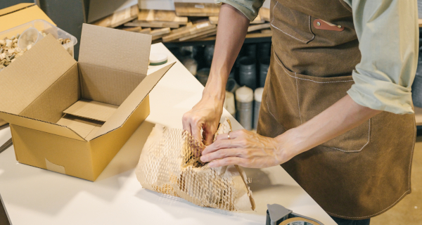 Decorative image for Reducing Plastic Pollution that shows a worker wrapping a product in brown paper for shipping