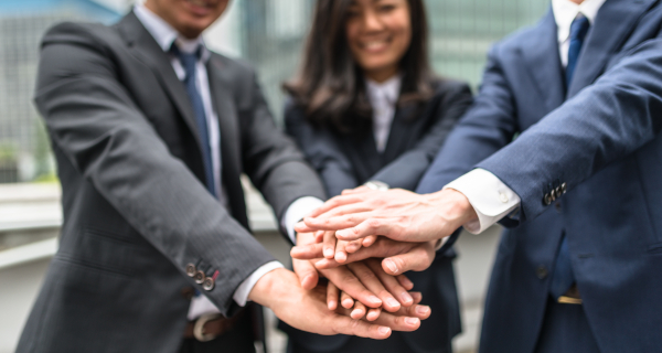 Decorative image for Responsible Business Conduct that shows three businesspeople in suits stacking their hands in the middle foreground